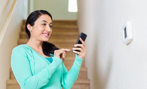 woman standing by thermostat using her phone to control it