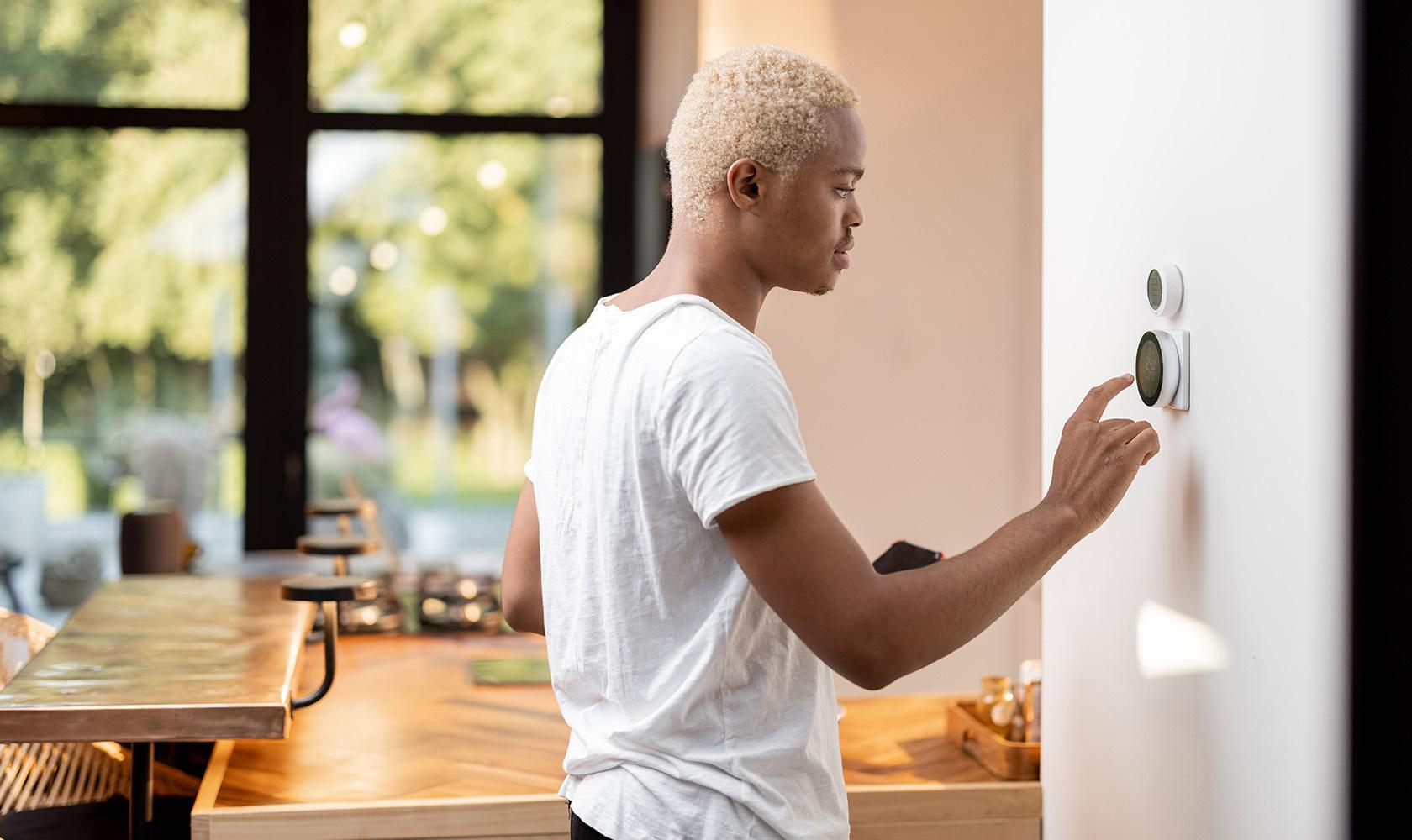 Young adult adjusts his smart thermostat. 