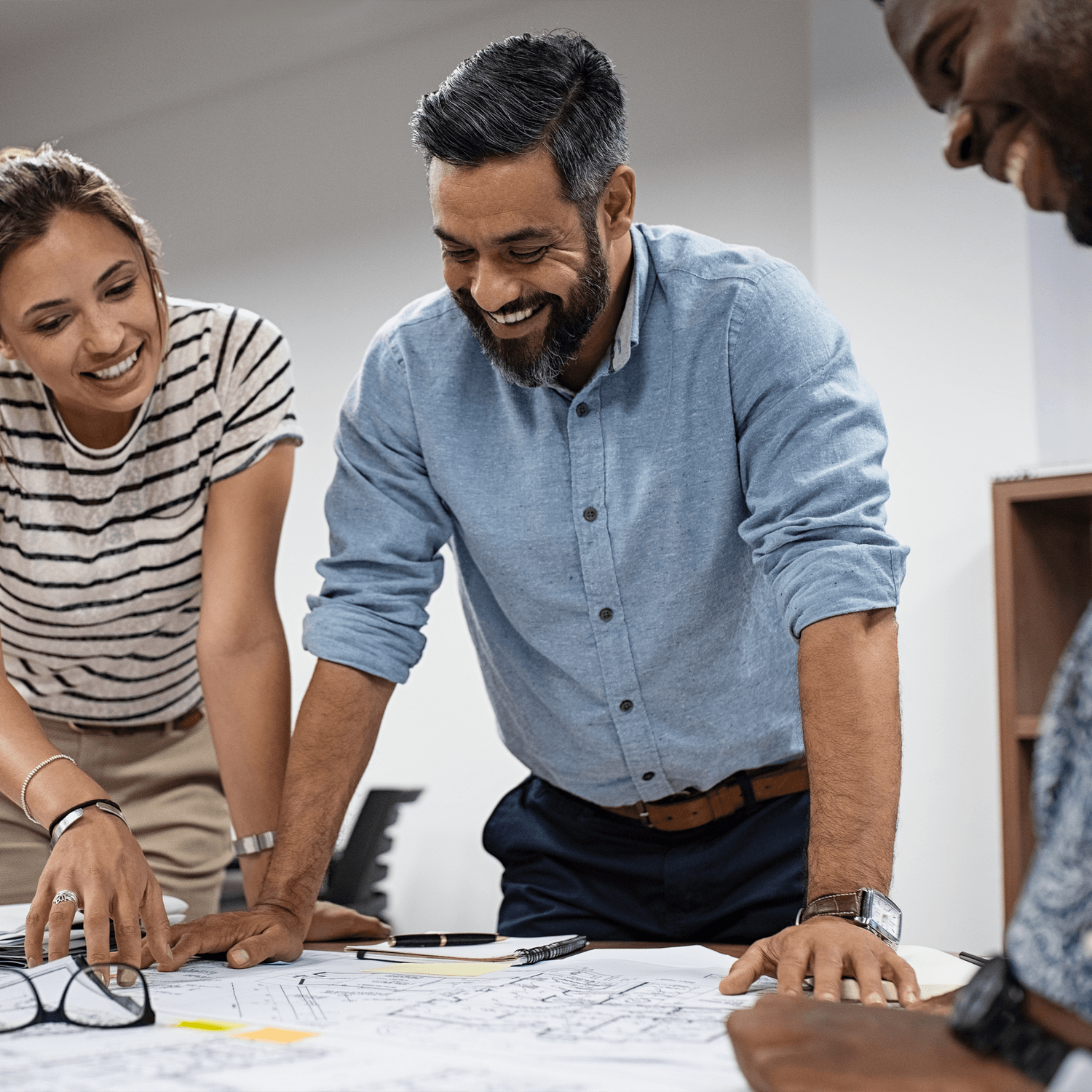 Man standing at desk overlooking blueprint, smiling